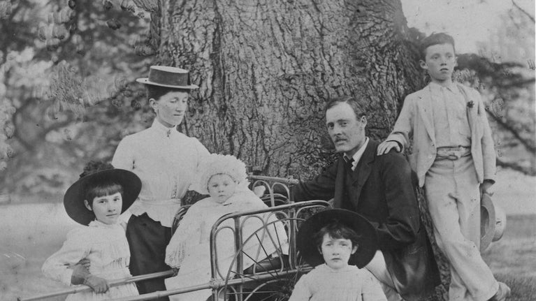 Black and white photograph of a family in a garden near a large tree trunk